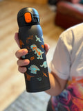 Zojirushi SM-WM48BA kids thermal mug 480 ml (16.20 oz) in black with colourful dinosaur design, reusable insulated travel bottle for hot and cold drinks, held in child’s hand indoors.